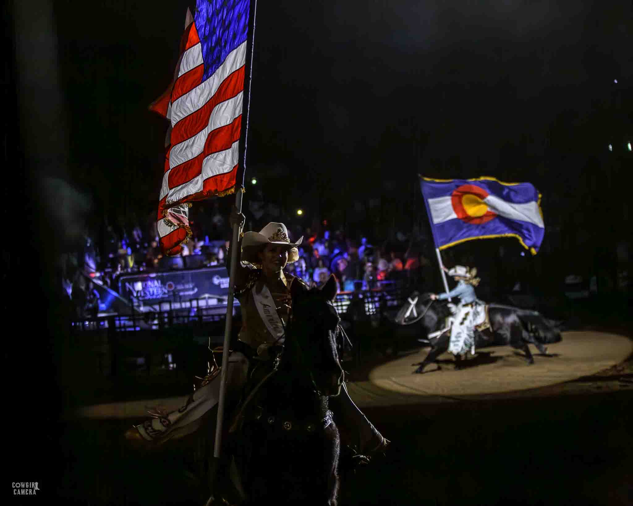 Dark arena with spotlights on the riders with the american flag and the Colorado flag